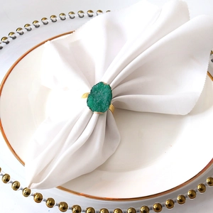 Close-up of a green agate stone napkin ring on white fabric with gold metal base