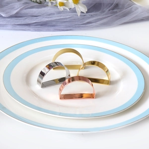 Set of four D-shaped metal napkin rings in gold, silver, and rose gold on a ceramic plate
