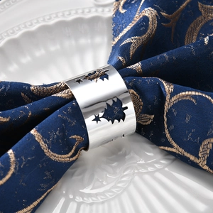 Silver hollow Christmas tree metal napkin ring on blue cloth and white ceramic plate