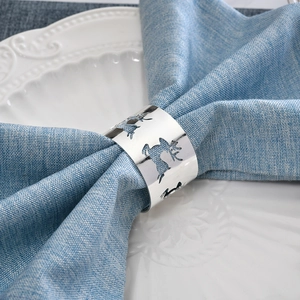 Polished silver Christmas reindeer napkin ring on blue linen over white embossed dinner plate