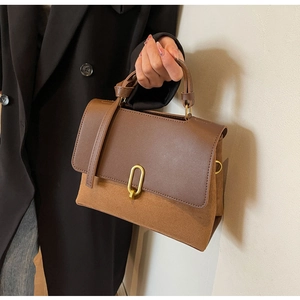 Detail of the brown leather and suede stitching with a gold oval clasp on the handbag