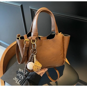 Détail d'un sac seau marron rétro en cuir texturé avec un pendentif de baseball
