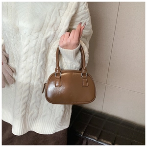 Detailed view of a brown glossy Boston handbag held by a model in a knit sweater