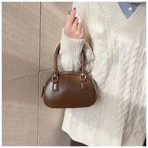 Detail of a brown leather bowling bag with top handles shown with a white knitted sweater