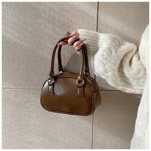 Close-up of brown Boston handbag with dual handles and silver metal hardware details