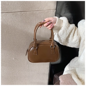 Close-up of a brown leather bowling handbag with double handles and a zipper closure