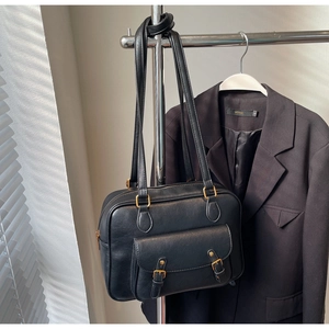 Detalle de bolso en cuero negro con hebillas doradas vintage y asas dobles de mano