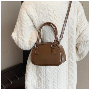 Brown semi-glossy leather bowling bag styled as a crossbody on a white knit sweater