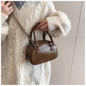 Close-up of a brown mini Boston bag in glossy faux leather worn with a white knit sweater