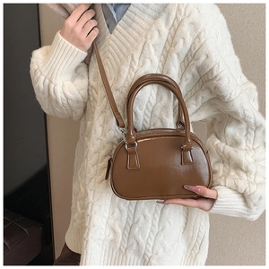 Close-up of a brown PU leather small square handbag styled with a white cable knit sweater
