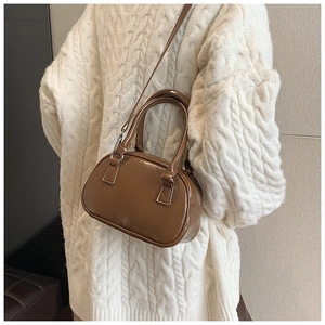 Close-up of a brown glossy leather bowling bag styled with a white knitted sweater