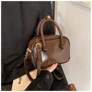 Dettaglio borsa in pelle lucida marrone scuro con manici sferici su blazer nero