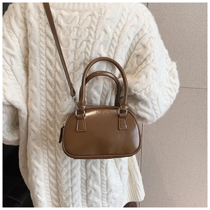 Close-up of a brown PU leather bowling bag with top handles and a thin crossbody strap