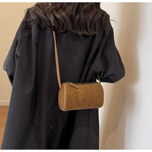 Deep brown suede cylinder bag worn crossbody over a black coat for a stylish look