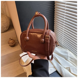 Dettaglio borsa in pelle marrone vintage con manico cilindrico e borchie dorate