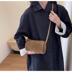Close-up of a brown suede Boston barrel bag worn as a crossbody on a navy blue shirt