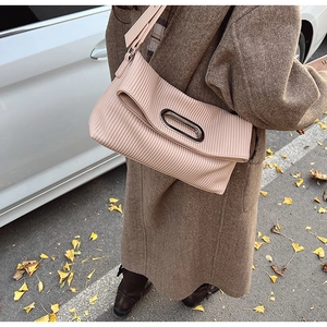 Detail of beige pleated handbag with metal handle in an autumn street setting