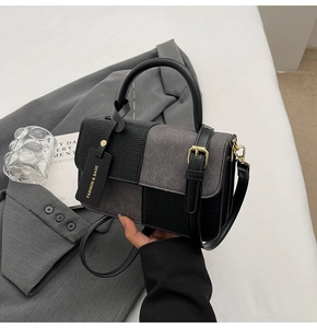 Detailaufnahme der Handtasche mit Kontrastfarben und goldener Schnalle auf grauem Sakko