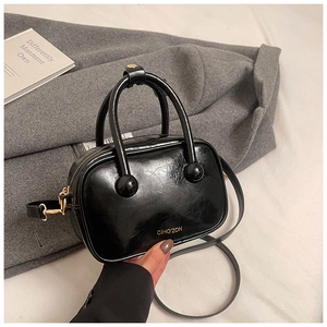 Dettaglio della pelle lucida nera effetto cracklé e logo dorato sulla borsa a tracolla