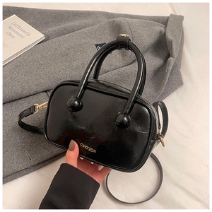 Dettaglio di una borsa in pelle verniciata nera con finiture dorate e logo del marchio