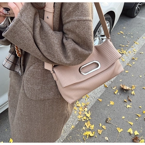 Detail of a dusty pink pleated shoulder bag with a silver oval clasp on a wool coat