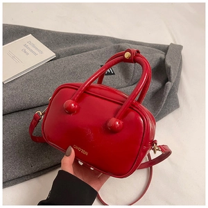 Dettaglio borsa rossa in pelle verniciata con logo dorato e accenti sui manici
