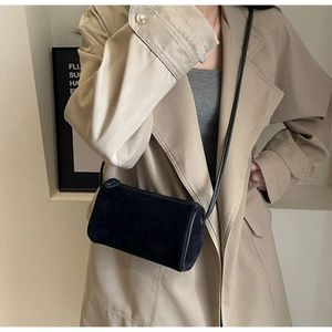 Detail view of a black matte cylinder crossbody bag worn with a khaki trench coat