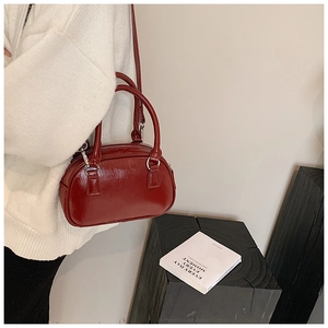 Detail view of deep red glossy leather bowling bag held by model in modern indoor setting