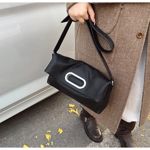 Detail shot of a black pleated crossbody bag with a silver oval metal buckle clasp