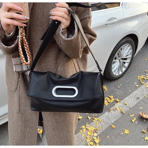 Macro detail of black pleated leather texture and oval silver metal buckle on shoulder bag