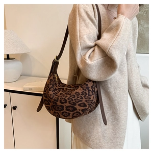 Detailed view of leopard print crescent bag featuring adjustable brown strap and gold zipper