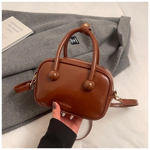 Dettaglio borsa marrone in finta pelle con borchie sferiche su sfondo cappotto grigio