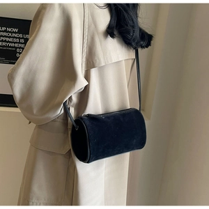 Detail view of black suede cylindrical Boston bag with slim leather crossbody strap