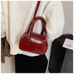 Detail of a glossy dark red bowling bag with silver hardware worn over a cream sweater