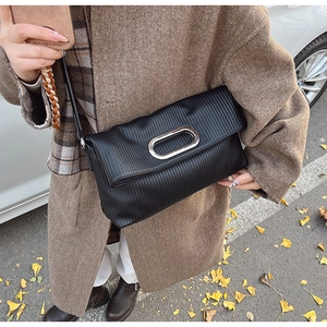 Detail of black pleated shoulder bag with silver metal accent worn with a wool coat