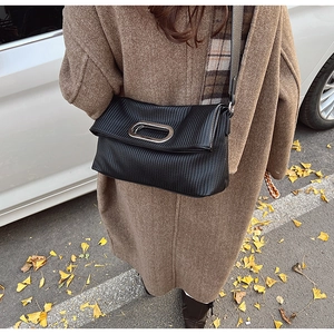 Detail of black pleated shoulder bag with silver oval metal handle in autumn setting