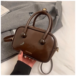 Dettaglio borsa in pelle cerata marrone con manico a sfera e logo del marchio