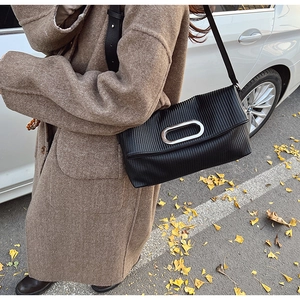 Detail of black pleated shoulder bag featuring a polished silver oval metallic buckle