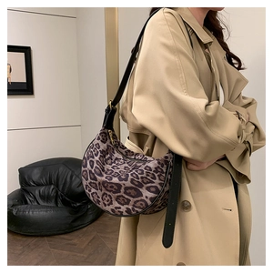 Close-up of leopard print crescent bag with leather strap worn over a khaki trench coat