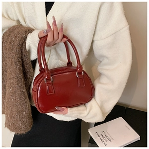 Detail of a dark red bowling handbag with silver metal rings and glossy leather finish