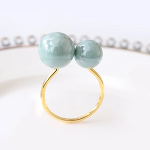 Detail of elegant gold napkin ring featuring two mint green pearls on a ceramic tray