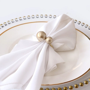 Close-up of elegant gold napkin ring with dual pearls on white fabric and ceramic plates