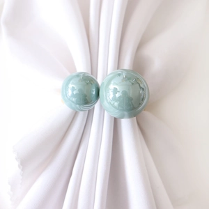 Modern teal U-shaped napkin ring with glossy pearls and gold metal accent on white fabric