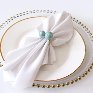 U-shaped gold napkin ring with Tiffany blue marble beads on white linen napkin