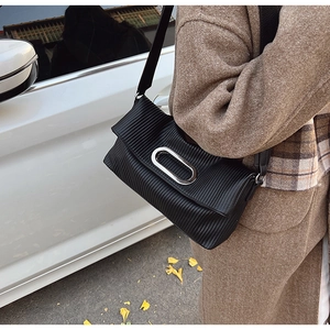 Detail of black pleated shoulder bag with a large silver oval buckle on textured fabric