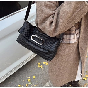 Detail of black pleated faux leather bag with large oval silver metallic buckle design