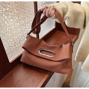 Detail of a brown pleated tote bag with a silver oval buckle held by a model