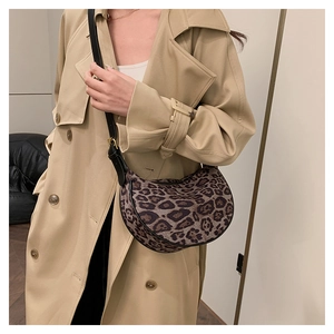 Close-up of leopard print crescent bag on trench coat showing strap and knit texture