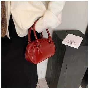 Detail of red bowling handbag with glossy finish and silver zipper shown on model