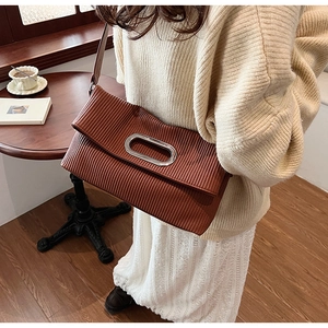 Brown pleated shoulder bag with silver oval metal handle shown in a cafe setting